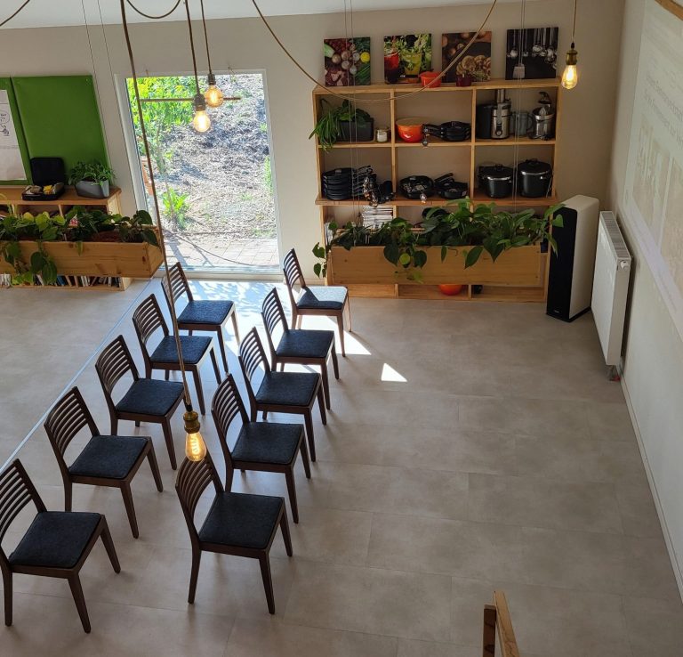 Stuhlreihen mit 10 Sitzplätzen in einem hellen Raum mit Pflanzen und Regalen im Hintergrund.