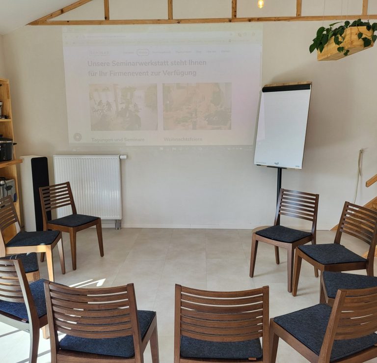 Besprechungsraum mit Stühlen im Kreis und Leinwand im Hintergrund.