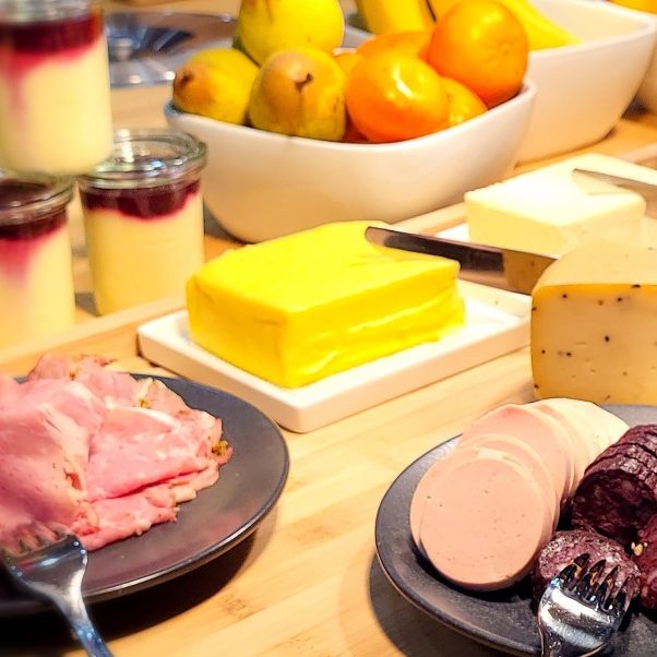 Verschiedene Käsesorten, Aufschnitt und frisches Obst auf einem Tisch präsentiert.