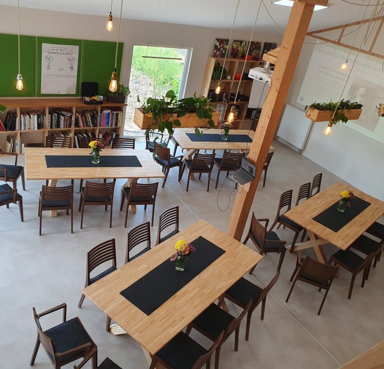 Helle, moderne Workshop-Atmosphäre mit Holztischen und Pflanzen, große Fenster.