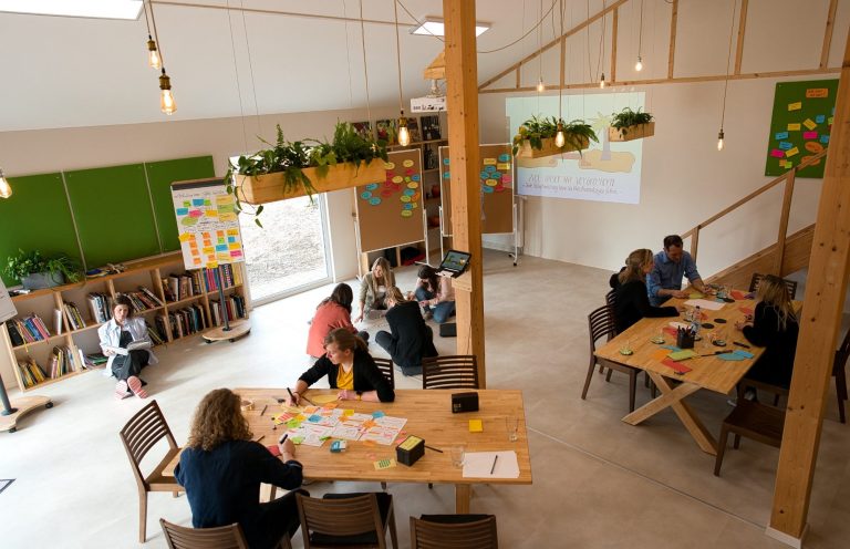 Pflanzen geschmückter Raum mit Menschen, die an Tischen arbeiten und brainstormen.