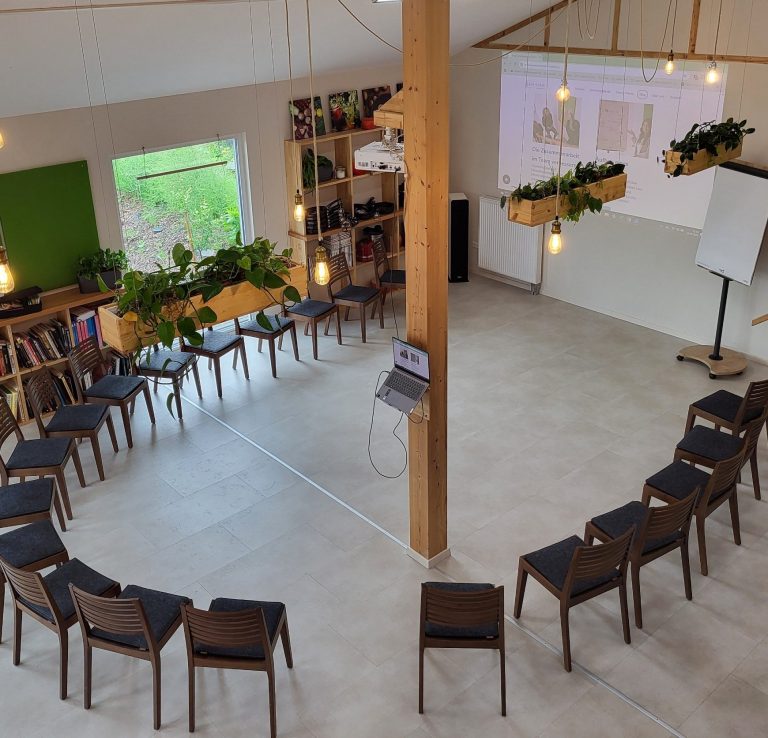 Seminarraum mit Stuhlkreis Stühlen, Pflanzen und Projektionsfläche an der Wand.
