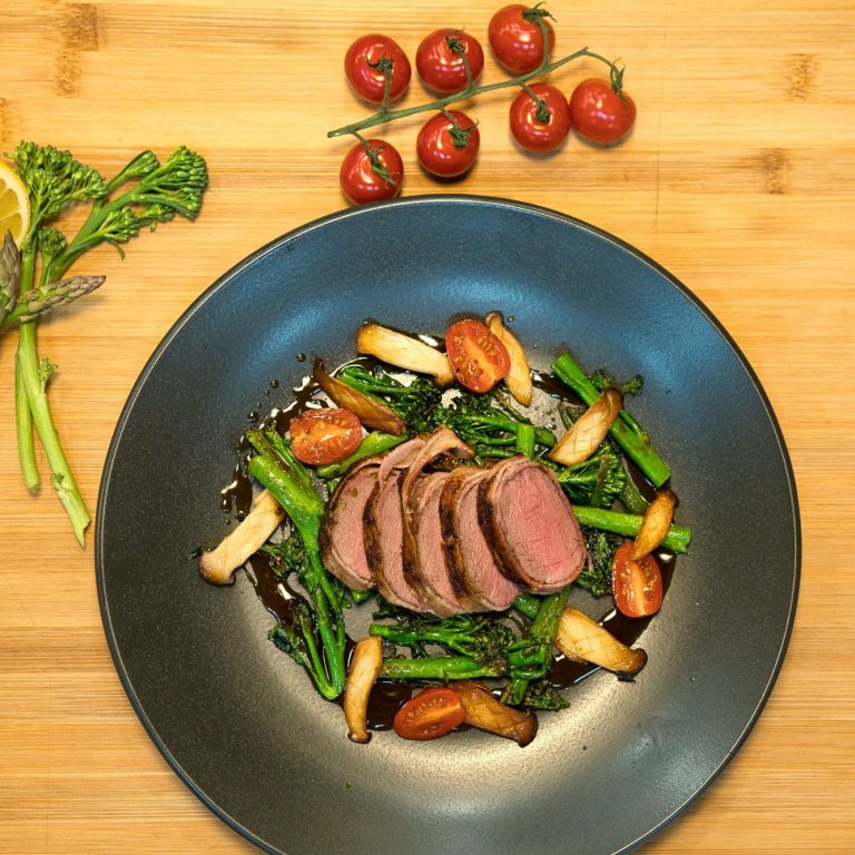 Rinderfilet mit grünem Gemüse und Kirschtomaten auf einem schwarzen Teller angerichtet.