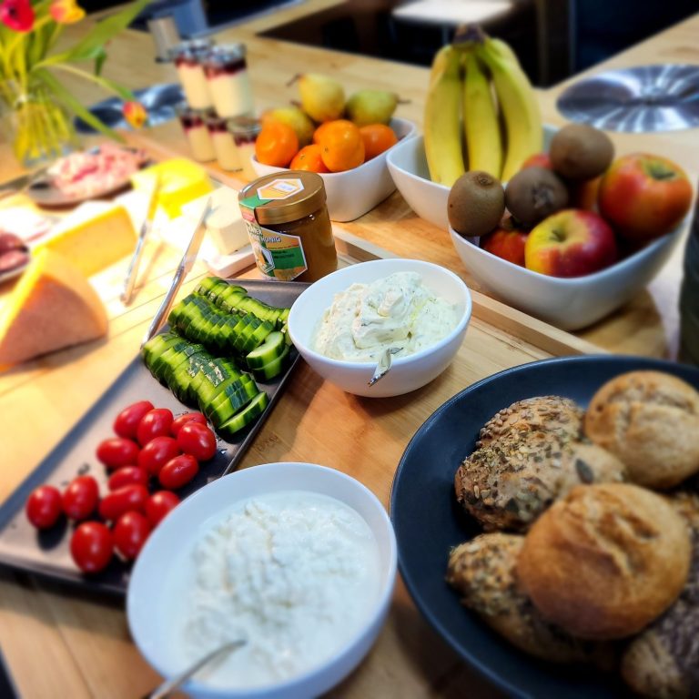 Ein Tisch mit frischem Obst, Gemüse, Joghurt, hausgemachten Brötchen und Käse.