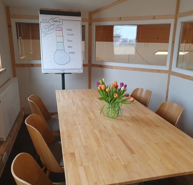 Ein heller Besprechungsraum mit einem großen Tisch, Stühlen und einer Blumenvase.