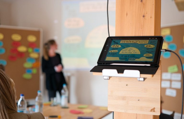 Person präsentiert Inhalte an einem großen Bildschirm, iPad im Vordergrund.