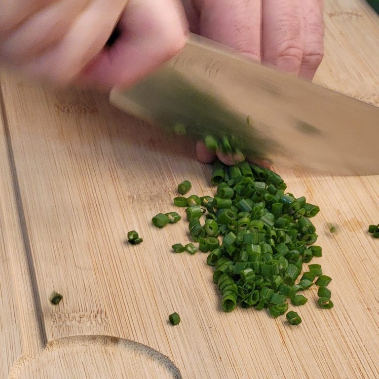Frisch geschnittene Frühlingszwiebeln auf einem Holzbrett.