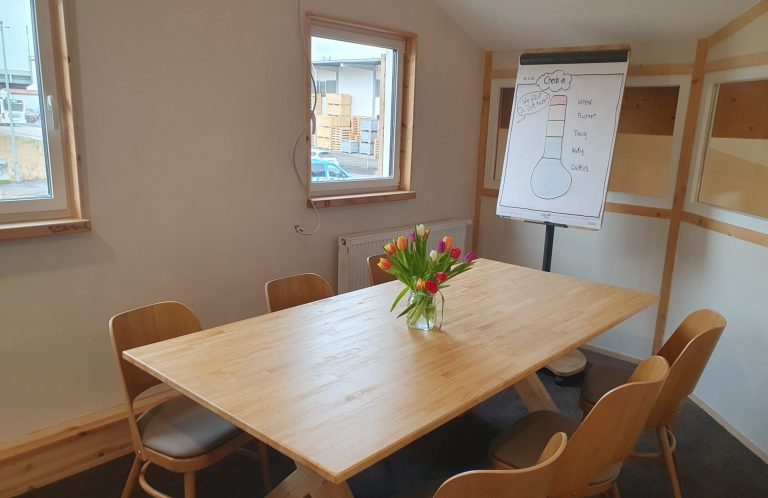 Ein sonniger Besprechungsraum mit einem Tisch, Stühlen und einem Flipchart.