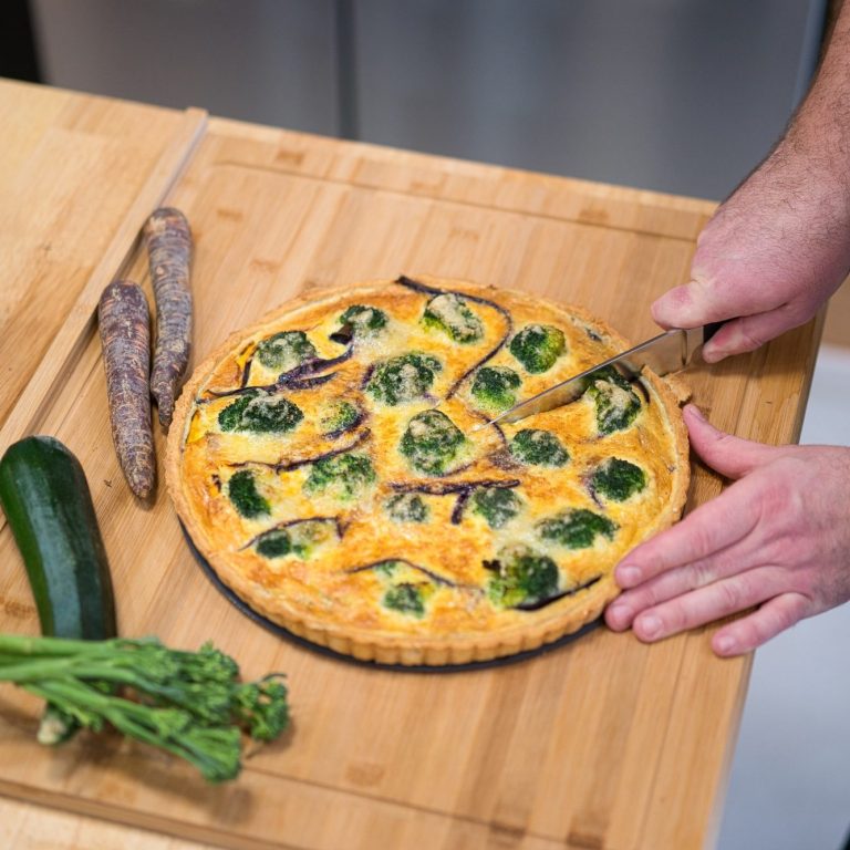 Eine Quiche mit Spinat und Zucchini, auf einem Holzbrett mit einem Messer geschnitten.